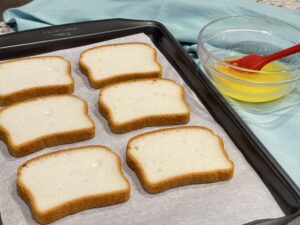 Image of gluten-free bread on a sheet pan with a bowl of melted butter and basting brush for the recipe: Easy Baked Gluten-Free Croutons