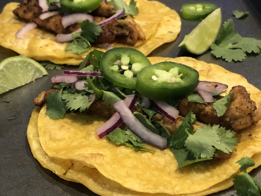 Image of corn tortillas layered with chicken, cilantro, onions, jalapenos, and a squeeze of lime for recipe: 15 Minute chicken Street Tacos.