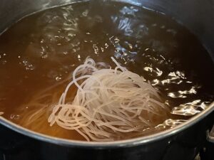 Image of rice noodles boiling in Fast Chicken Pho broth.